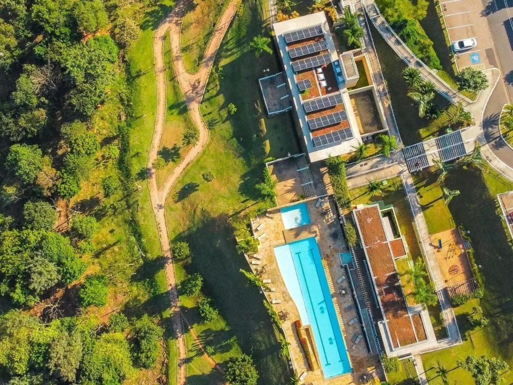 Vista aérea de condomínio horizontal com área verde, piscina e estrutura de lazer integrada ao entorno residencial.