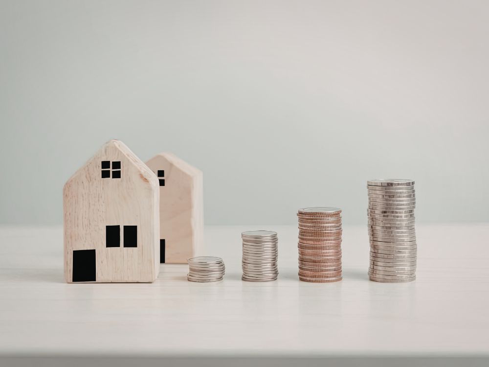 Casas em miniatura ao lado de pilhas de moedas demonstrando quanto valoriza um imóvel por ano em investimentos.