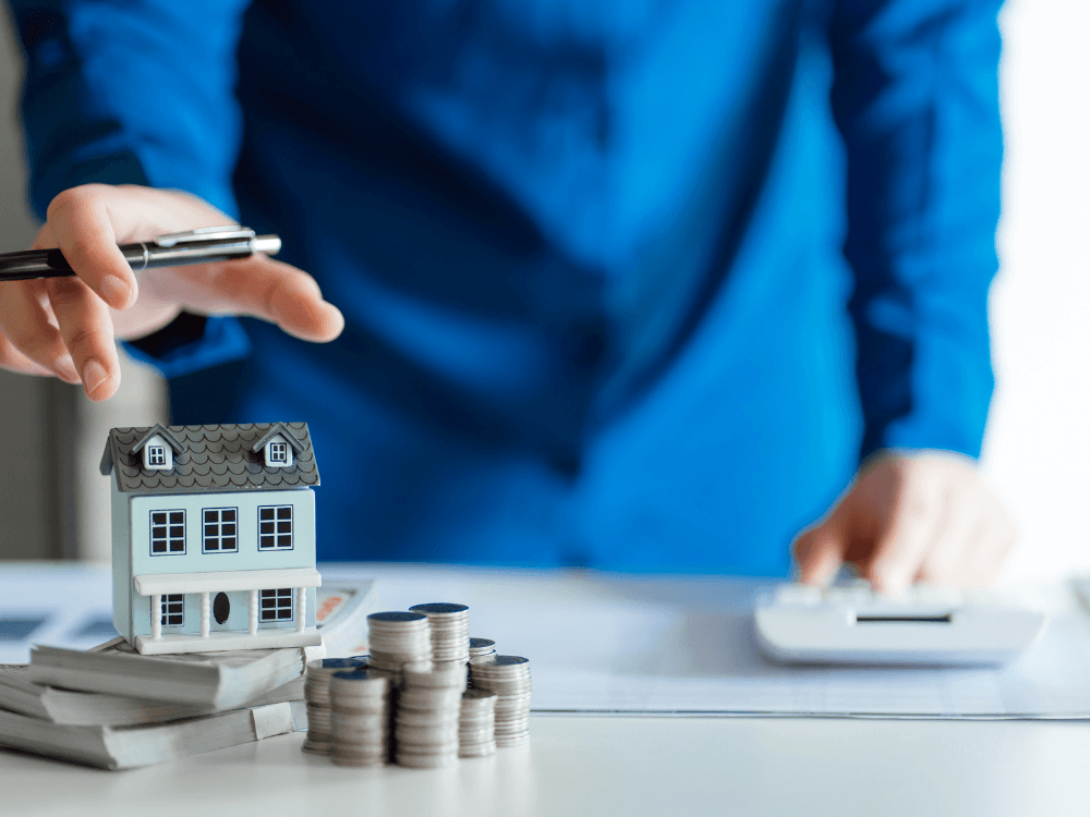 Miniatura de casa, moedas e documentos sobre a mesa representam a avaliação imobiliária para definir o preço de venda.