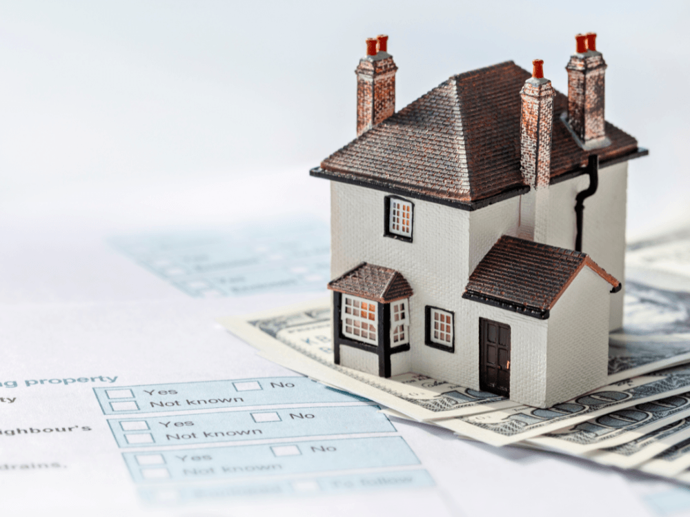Maquete de casa sobre documentos e cédulas representa avaliação, precificação e valor de mercado de imóveis de alto padrão.