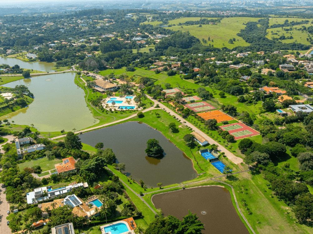 Vista aérea de condomínio residencial cercado por áreas verdes, lagos, piscinas e quadras para lazer dos moradores. Tudo para explicar as vantagens de morar em um condomínio de luxo