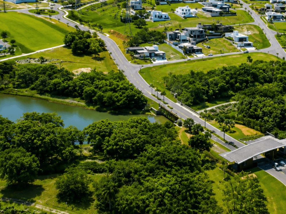 Entrada de condomínio de luxo com acesso estruturado, vias internas, paisagismo e residências de alto padrão ao redor