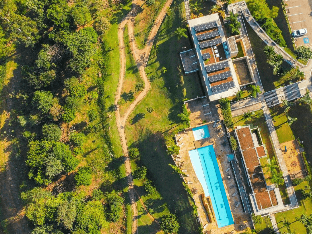 Vista aérea de condomínio horizontal com áreas verdes, piscina, casas e caminhos internos entre a vegetação.