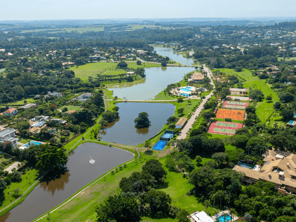 Vista aérea de complexo residencial com lagos, áreas verdes, piscinas e quadras esportivas distribuídas pelo condomínio.