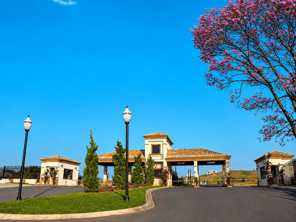 Entrada de condomínio horizontal com guaritas, portões, vias pavimentadas, jardins e iluminação na área de acesso residencial. Tudo para explicar o que é um condomínio horizontal.